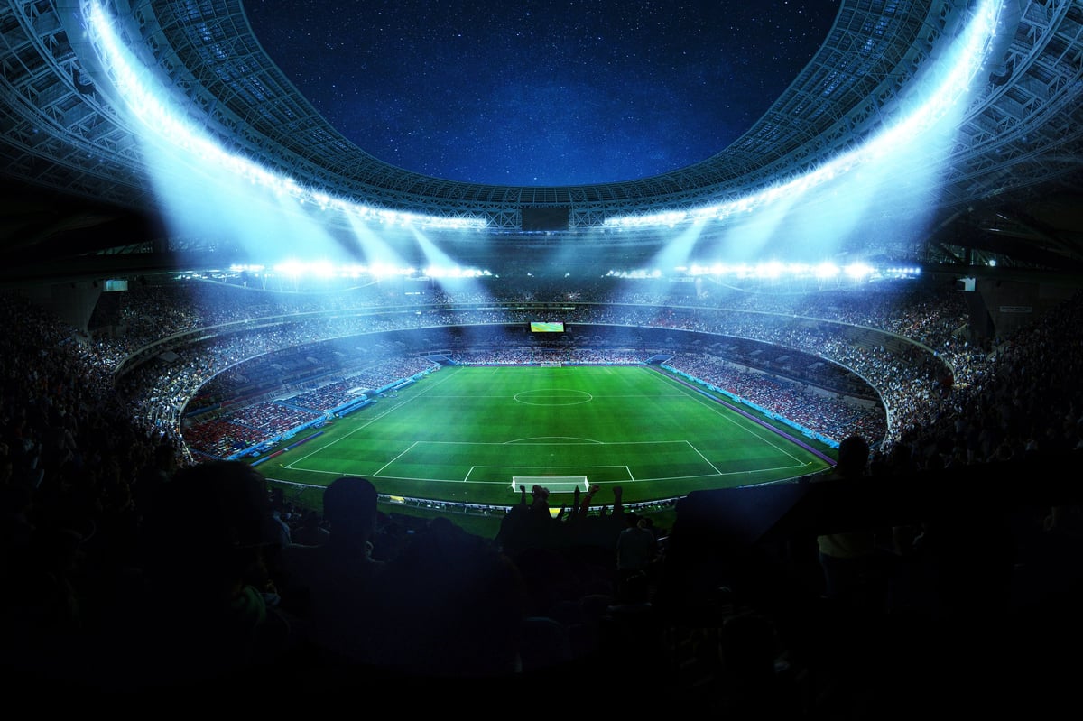 Floodlit sports stadium packed with fans under the night sky